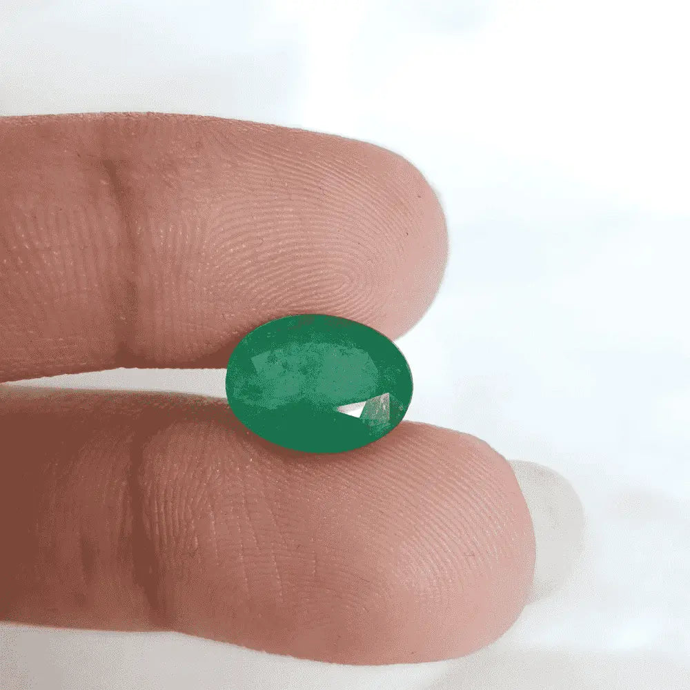 Hand holding a polished natural emerald stone for sale, featuring a vibrant green color and smooth finish