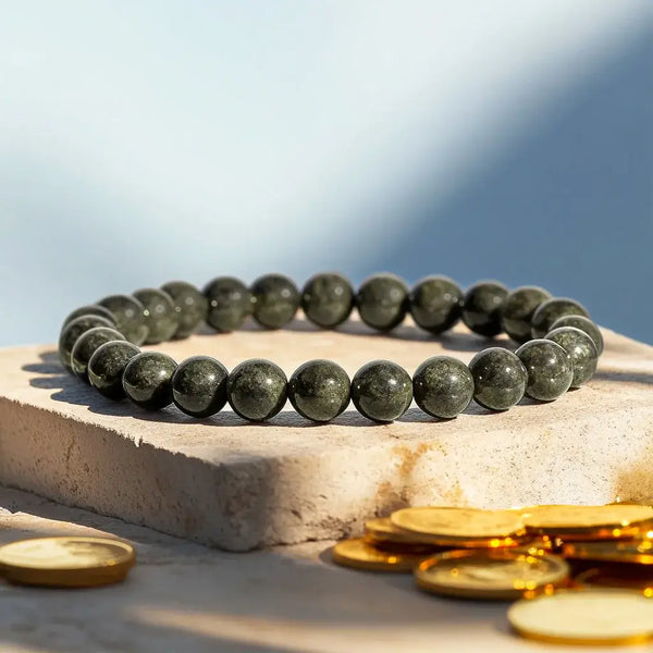 Green beaded bracelet on a stone surface with gold coins